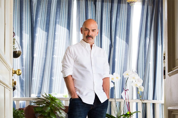 The Orchid Wrangler Michael Simon standing next to a white orchid in front of blue curtains.