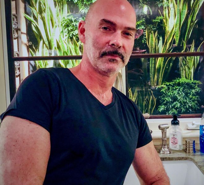 Michael Simon in posing in a kitchen with plant arrangements in the window behind him.