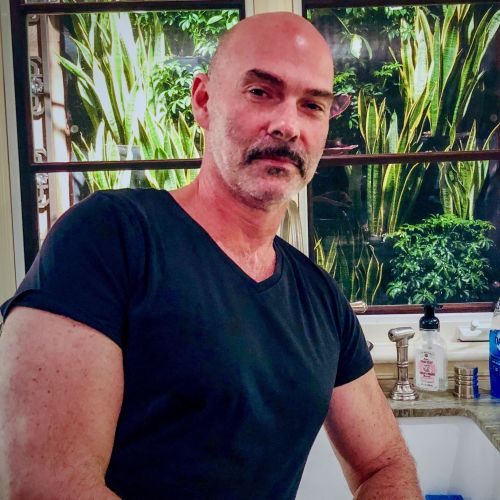 Michael Simon in posing in a kitchen with plant arrangements in the window behind him.